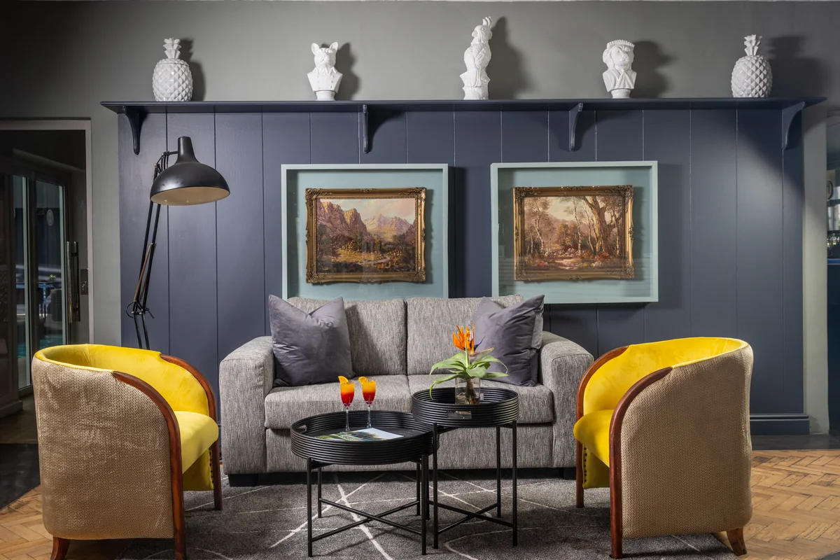 Lounge with yellow tub chairs and landscape paintings at Majeka House Boutique Hotel