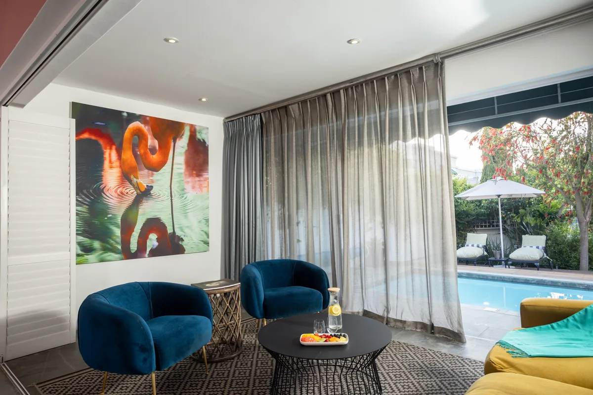 Pool Suite lounge with velvet chairs, flamingo canvas and doors open to the pool at Majeka House Boutique Hotel