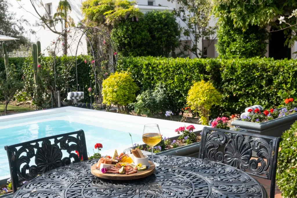 Platter and a glass of wine on a garden table beside the pool at Majeka House Boutique Hotel