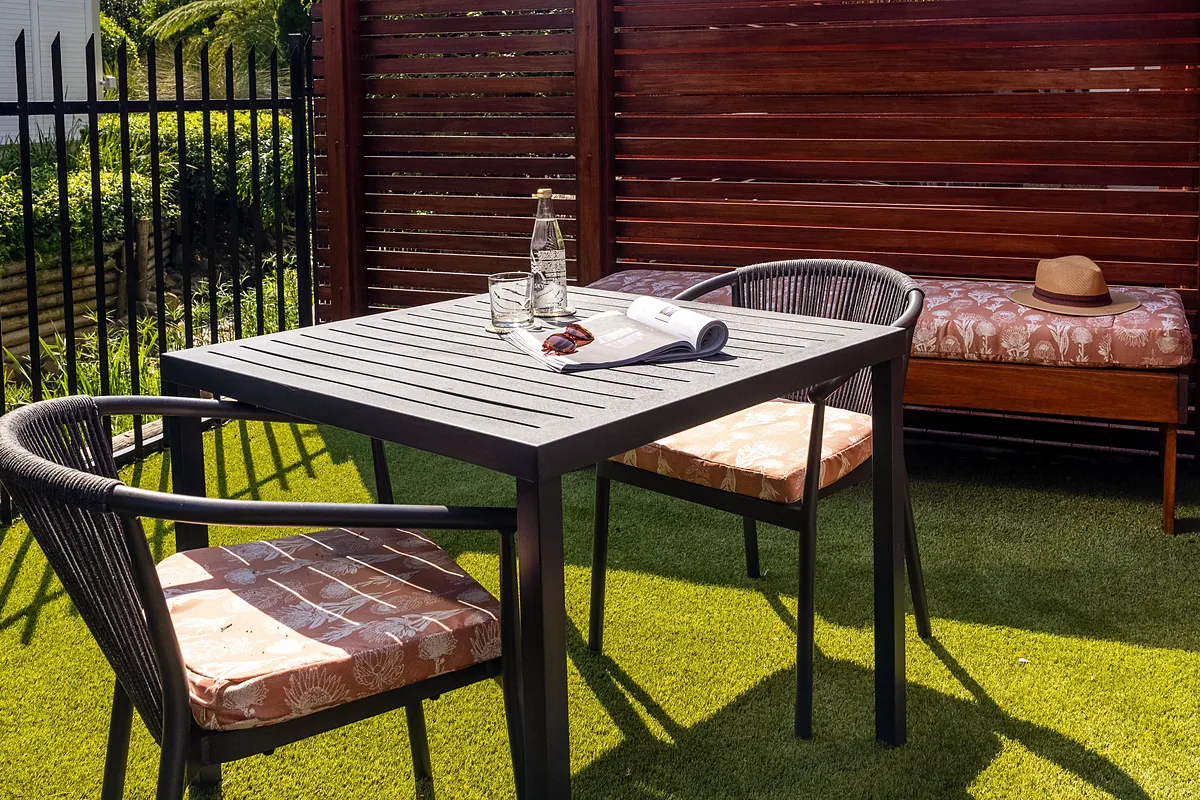 Private garden patio with a table, two chairs and a cushioned bench at Plumwood Boutique Hotel
