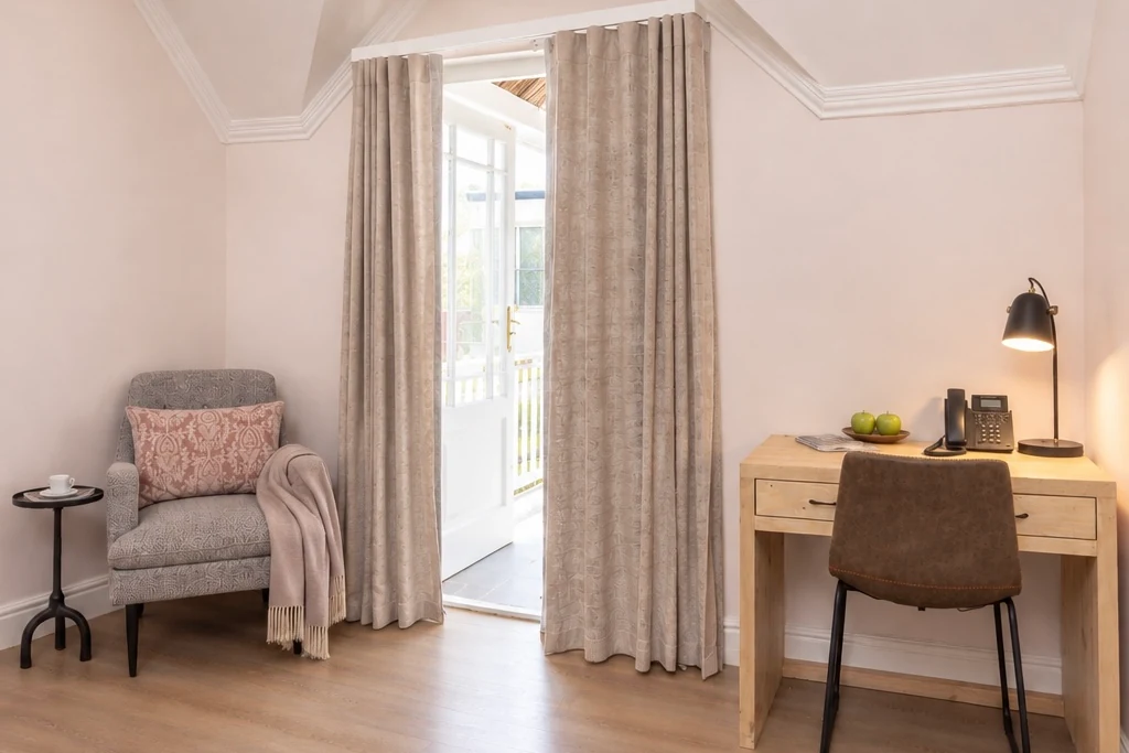Armchair, desk and the door to the private balcony in a Deluxe Room at Plumwood Boutique Hotel