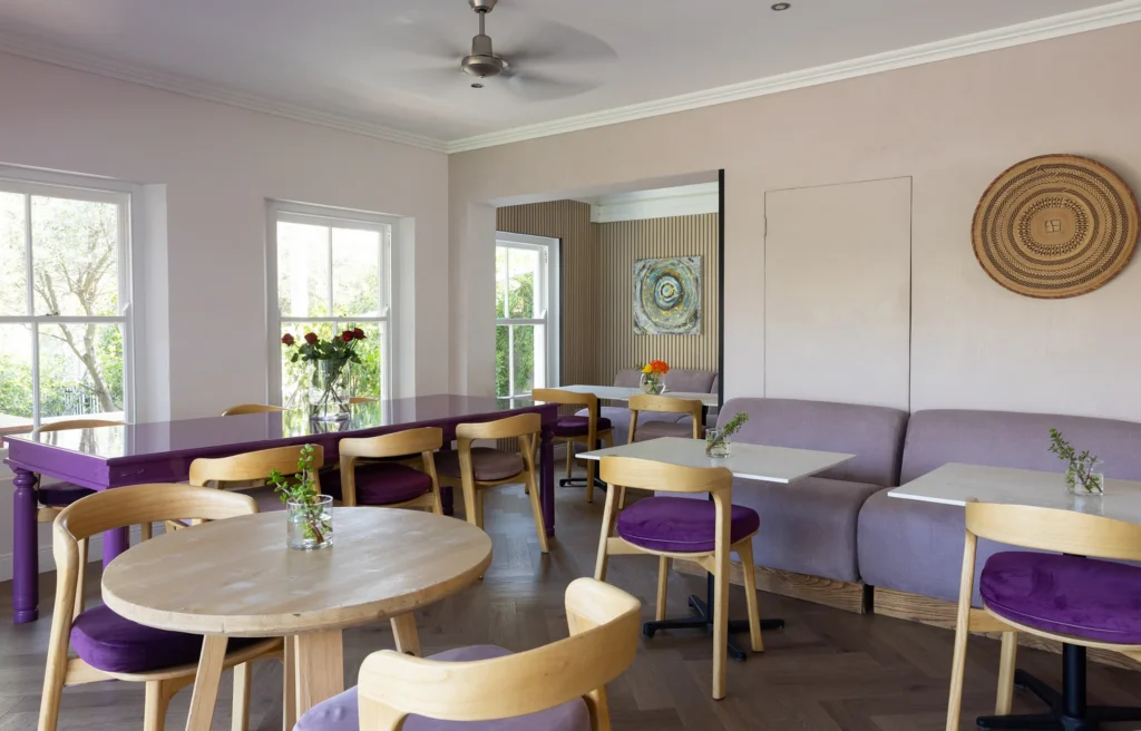 Dining room with a purple table, wooden chairs and a lilac banquette at Plumwood Boutique Hotel
