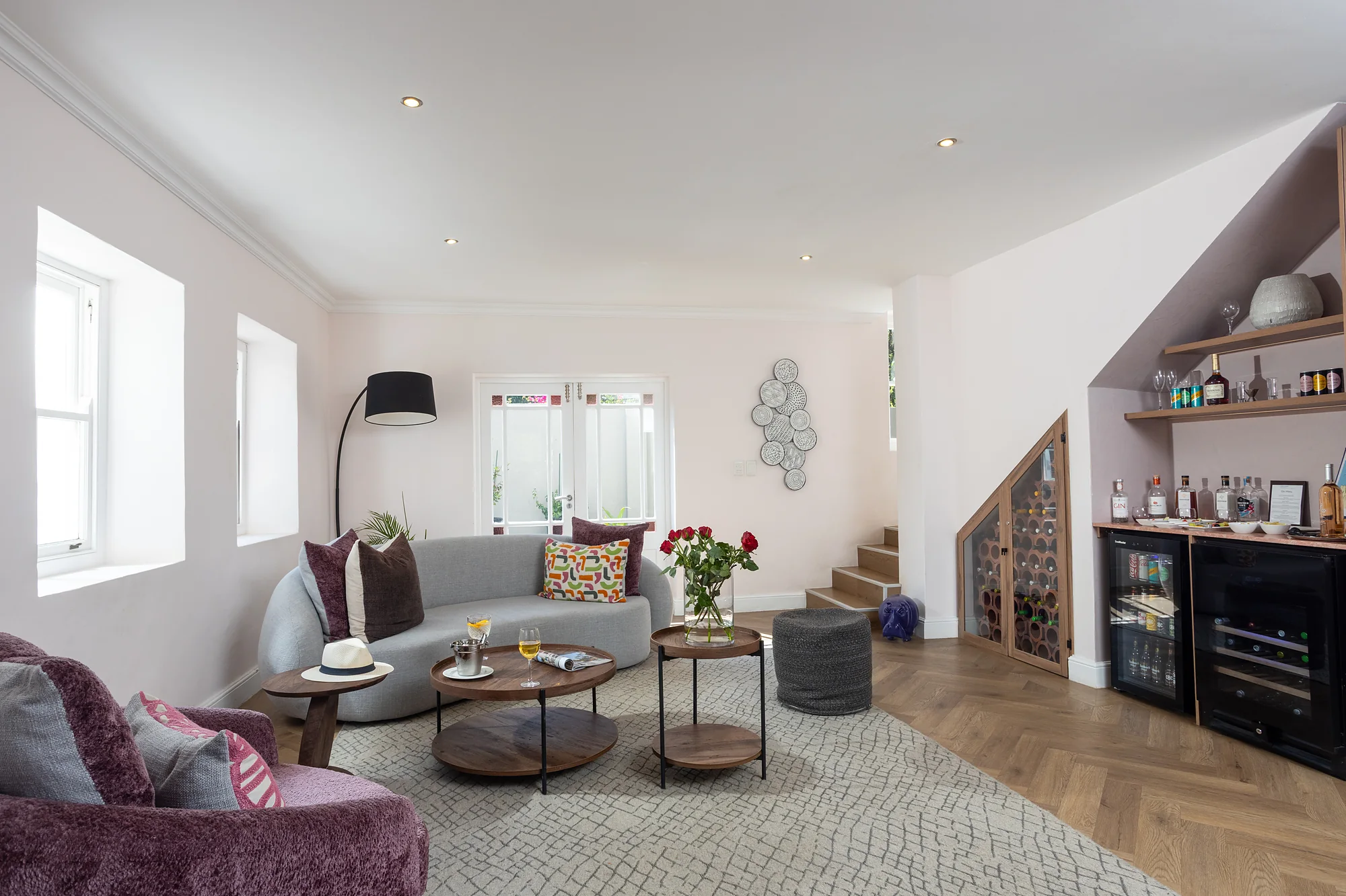 Guest lounge with a grey sofa, coffee tables and a bar under the stairs at Plumwood Boutique Hotel